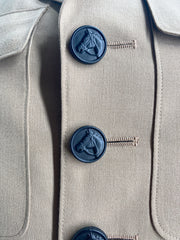 A textured close-up of a jacket, highlights three round, matte black buttons. Each button features a detailed, raised design of a horse's head in profile. The buttons are vertically aligned, with visible stitching securing them to the fabric. The overall image emphasizes the texture and craftsmanship of the garment.