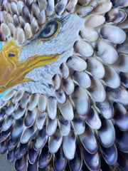 A close-up view of 'Bird of Prey,' an 8" diameter circular mixed media artwork by Shireen Renee depicting the profile of a bald eagle head with a striking combination of oil-painted beak and eye, surrounded by textured coquina shell feathers.