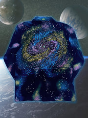 A close-up studio shot of a dark blue, collared jacket with a full zipper. The jacket features a vibrant, abstract pattern of colorful splotches and dots in blue, purple, yellow, and white, creating a galaxy-like effect. The jacket is presented against a digital backdrop of space, with two planets visible in the background. This is an Art Of Uniformity brand jacket by Shireen Renee.