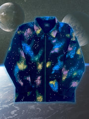 A close-up studio shot of a dark blue, collared jacket with a full zipper. The jacket features a vibrant, abstract pattern of colorful splotches and dots in blue, purple, yellow, and white, creating a galaxy-like effect. The jacket is presented against a digital backdrop of space, with two planets visible in the background. This is an Art Of Uniformity brand jacket by Shireen Renee.
