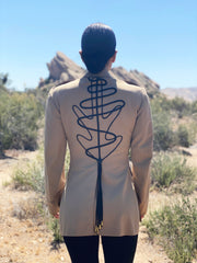 Model standing in a desert environment wearing a vintage American USMC khaki jacket with hand-embroidery line art on the back and gold-tipped tassels at the back vent. There are rock formations in the distance.