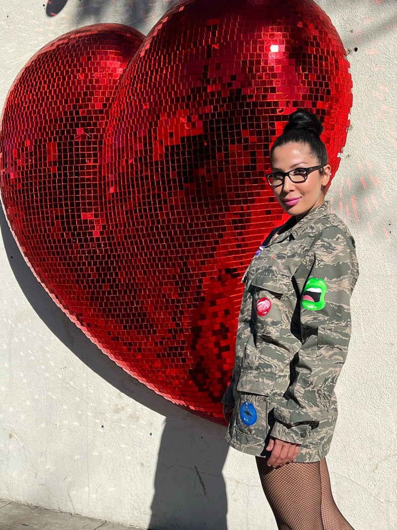 Model wearing a vintage American camo jacket with hand-painted pop lip art standing in front of a giant red heart.