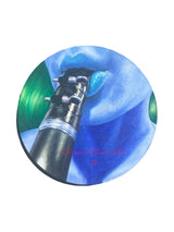 "The Lullaby" is an oil painting on an 8" circular canvas depicting a close-up view of the artist, Shireen Renee, playing the clarinet. Her skin tone is painted in blue hues and her hair in green hues.
