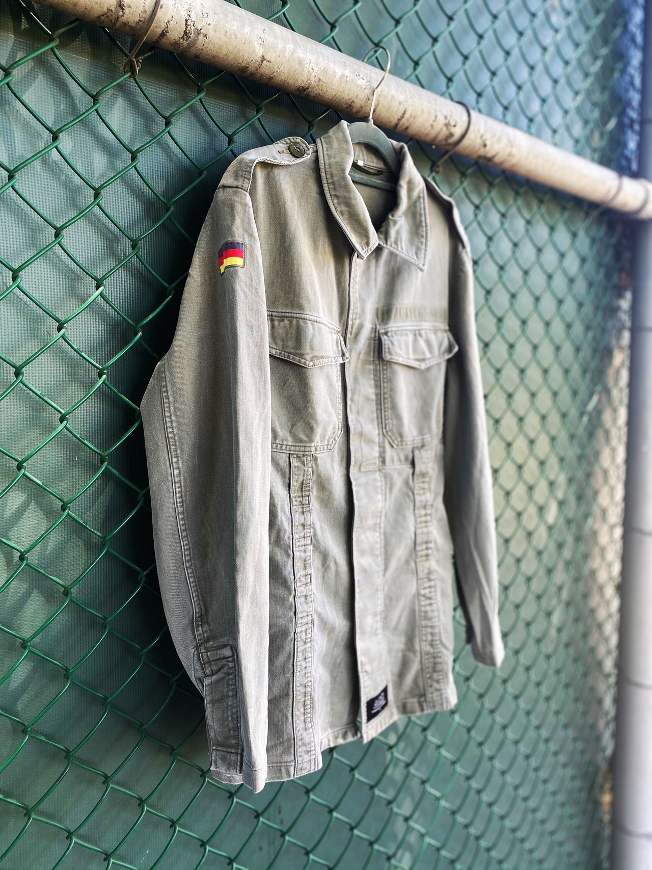 Artwear gummy bear jacket hanging on a chain link fence with back of jacket showing. Jacket showcases a giant, painted green gummy bear by Los Angeles artist, Shireen Renee.