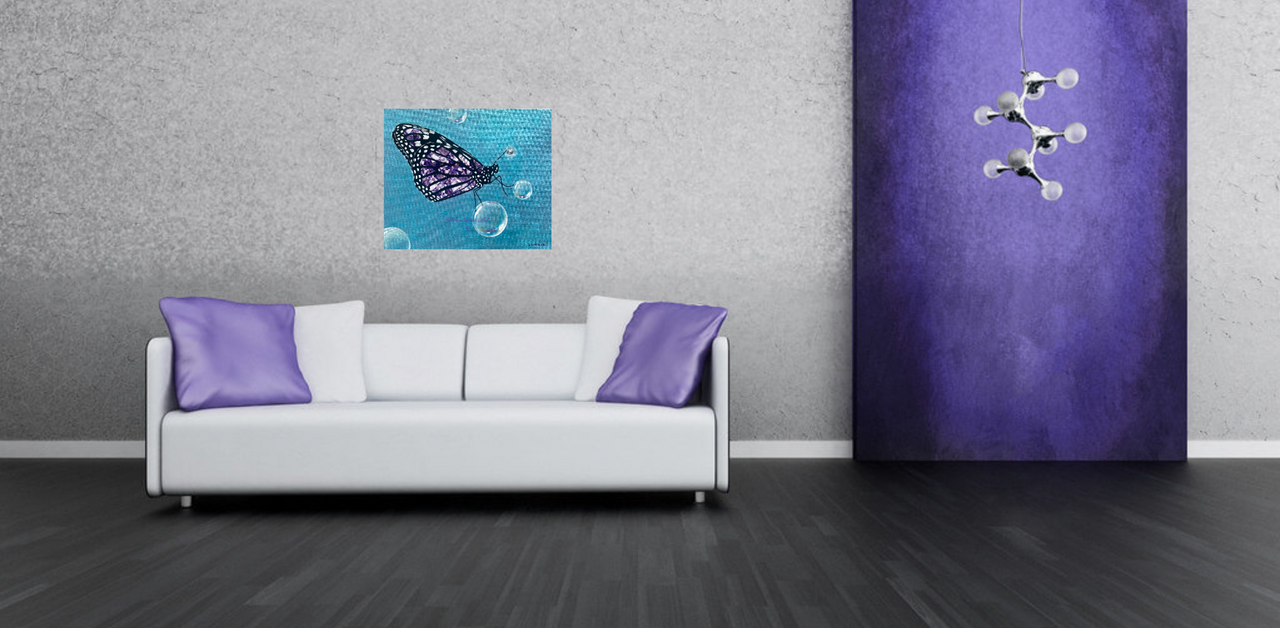 A white sofa with purple pillows sits on a dark floor beneath Shireen Renee's Metamorphosis butterfly painting on a light gray wall. The painting features a stylized butterfly with intricate purple amethyst wings, surrounded by several translucent bubbles against a light blue, textured background. To the right, a textured purple panel has a modern, multi-bulb white light fixture extending from it.