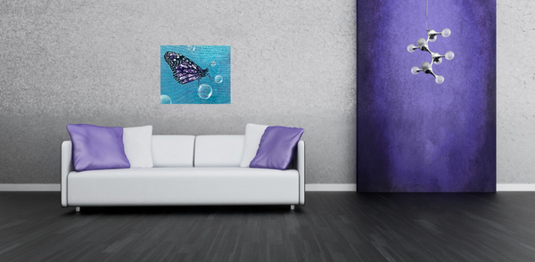 A white sofa with purple pillows sits on a dark floor beneath Shireen Renee's Metamorphosis butterfly painting on a light gray wall. The painting features a stylized butterfly with intricate purple amethyst wings, surrounded by several translucent bubbles against a light blue, textured background. To the right, a textured purple panel has a modern, multi-bulb white light fixture extending from it.